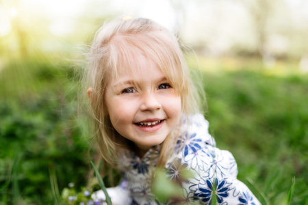 Little smiling girl with spring flowers on green lawn in the garden. High quality photoの写真素材