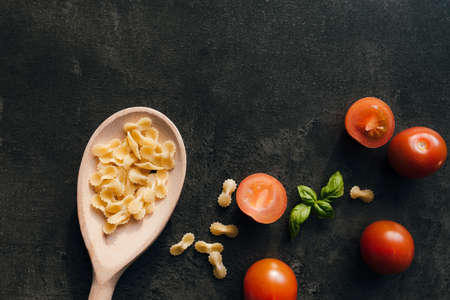Red cherry tomatoes, green basil, butterfly vermicelli pasta, wooden spoon on gray background. High quality photoの写真素材