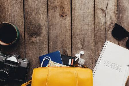 Flat lay travel concept with passports, black wallet, hand bag, protective mask and sanitizer, notepad and earphones, eyeglasses, cup of coffee, photo camera on wooden background. High quality photoの写真素材