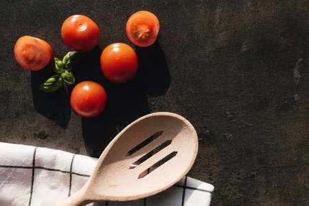 Red cherry tomatoes, green basil, wooden spoon, towel on gray background. High quality photoの写真素材