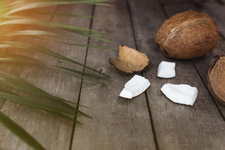 Broken coconuts on gray wooden background with palm leaf. White coconut pulp. High quality photoの写真素材