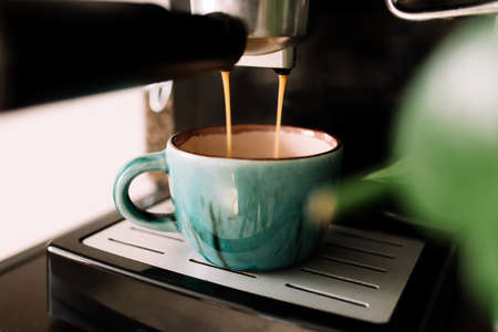 Green cup of coffee at the coffee maker machine, coffee time. Blurred background. High quality photoの写真素材