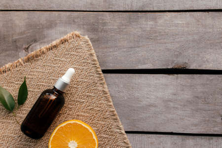 Orange essential oil in glass bottle with green leaf. Cosmetic concept on wooden background on sackcloth, isolated flat lay. High quality photoの写真素材