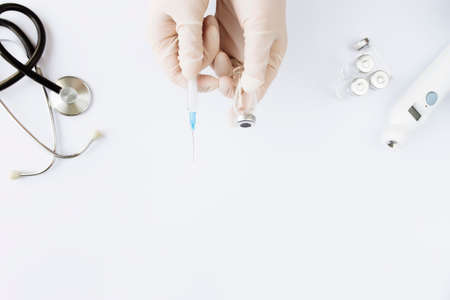 Medicine treatment, vaccination concept. Doctor hands holding bottle with vaccine and injection syringe, electronical thermometer, stethoscope and vaccine vial on white background. High quality photoの写真素材