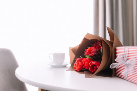 Red tulips bouquete on table, white coffee cup. Concept for greeting card for mothers day,...