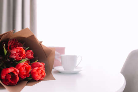 Red tulips bouquete on table, white coffee cup. Concept for greeting card for mothers day, international womans day or valentines day concept, birthday greeting conceptの写真素材