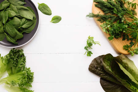 Flat lay with cutting board and bowl of fresh green salad leaves of spinach and lettuce, romaine and parsley, basil on white background. Healthy vegetarian eating concept. High quality photoの写真素材