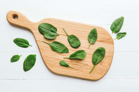Wooden cutting board with fresh green salad leaves of spinach on white background. Healthy vegetarian eating concept. High quality photoの写真素材