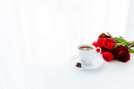 Red tulips bouquete on table, white coffee cup. Concept for greeting card for mothers day, international womans day or valentines day concept, birthday greeting concept, dark chocolate candyの写真素材