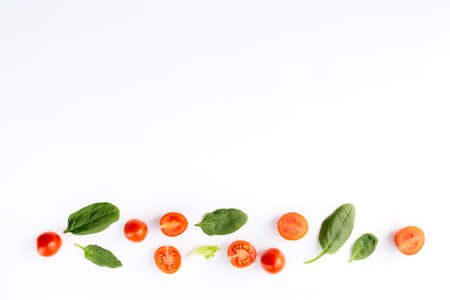 Flat lay with red cherry tomatoes and green spinach leaves on a white background. Healthy eating concept. High quality photoの写真素材