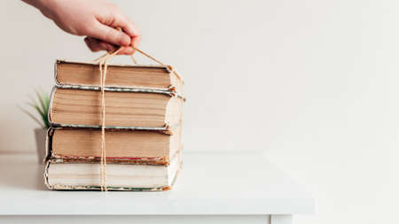 Hand holding a stack of old books in the library, concept of learning, study and education, concept of science, wisdom and knowledge. High quality photoの写真素材