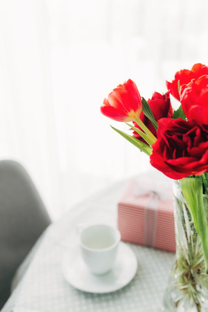 Red tulips bouquete on table, white coffee cup. Concept for greeting card for mothers day, international womans day or valentines day concept, birthday greeting conceptの写真素材
