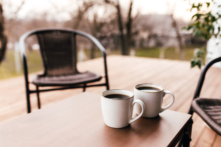 Two cups of coffee on the table on the wooden brown terrace during evening sunset. Relaxation,...