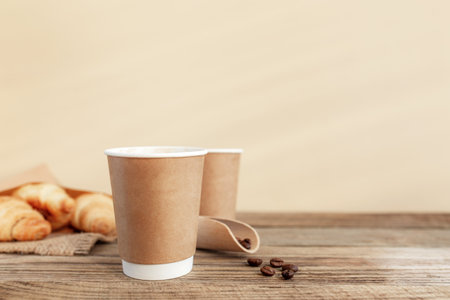 Two paper cups of coffee, croissants, coffee beans and spoon at wooden tableの写真素材