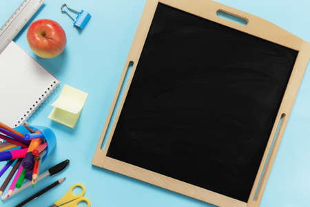 Flat lay with school concept on blue background with various schooling accessories, pens, pencil, notepad, paper clips, apple, ruler, scissors, empty black board, paper sticker on blue backgroundの写真素材