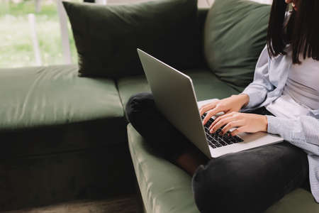 A brunette girl sits on a green sofa and prints or typing something on a laptopの写真素材