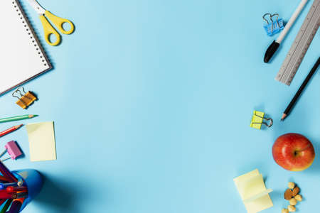 Flat lay with schooling, work or educational concept with various school accessories, pens, pencil, notepad, paper clips, apple, nuts, ruler, scissors, paper sticker on blue backgroundの写真素材