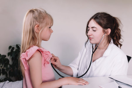Doctor or nurse in white uniform examining and listening small girl using stethoscope in the clinic during doctor visit. High quality photoの写真素材