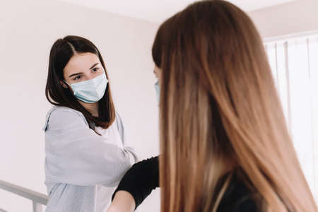 Two smiling girls in protective face mask say hello with elbowの写真素材