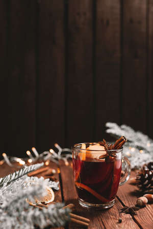 Christmas time concept photo. Glass cup or mug with Mulled Wine inside on wooden table background. Decorations, cinnamon, dried orange, apple, various spices, white fir, cone, anise, aniseed, lightsの写真素材