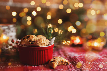 Red festive bowl full with Christmas cookies, blurred Christmas fir tree lightsの写真素材