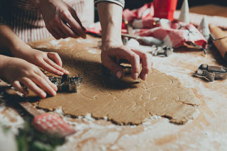 Merry Christmas, Happy New Year. Gingerbread cooking, baking. Mom and daughter make cookies, cut out different shapes of cookies using cutting metal mold on wooden table at kitchen. High quality photoの写真素材