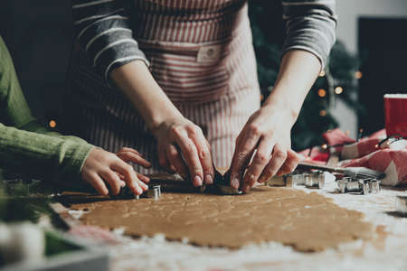 Merry Christmas, Happy New Year. Gingerbread cooking, baking. Mom and daughter make cookies, cut out different shapes of cookies using cutting metal mold on wooden table at kitchen. High quality photoの写真素材