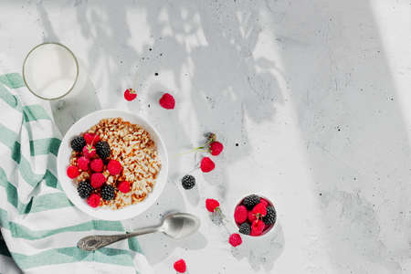 Morning healthy breakfast, white bowl full with granola, muesli, raspberry, blackberry on gray concrete table. Healthy eating, eco, bio food concept. Fresh tasty meal on grey background. Quality photoの写真素材