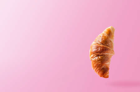 Freshly baked croissant levitating or flying. Croissant fly in the air isolated on pink background. Levitation scene. Copy space place. Signboard mockup or advertisement of bakery, confectioneryの写真素材