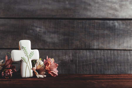 Easter holiday conceptual background on rustic wooden boards. Photo of white gingerbread cookie Cross shape, flowers bouquet on table top. Card with copy space to place text. Minimal conceptの写真素材