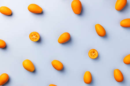 Light blue flat lay with top view on fresh ripe orange cumquat or kumquat citrus. Full, cut and sliced fruits. High quality pattern photo. Healthy eating concept. Vegan or vegetarian eating foodの写真素材