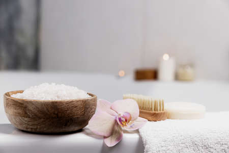 Preparation for hotel spa treatment, home bath procedure. White washbasin in bathroom, accessories on tray. Burning candles, soap, foot brush, towel, glass bottle with sea salt, orchid flowerの写真素材