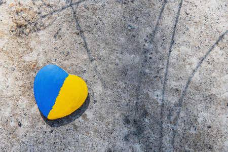 Stone in shape of a heart painted with the Ukrainian flag lies on the ground or concrete. No war. Stop the war, the genocide of Ukrainians. Flat lay with copy space. Save Ukraine people from invasion.の写真素材