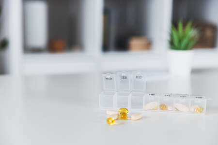 Closeup of medical pill box with doses of tablets for daily take a medicine with white, yellow drugs and capsules used for treatment, cure the disease. Healthy lifestyle, vitamins, omega-3 supplementsの写真素材