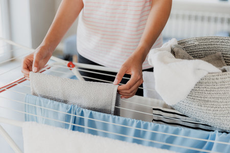 Woman hanging clean wet clothes laundry on drying rack at home laundry room. Detail of female...