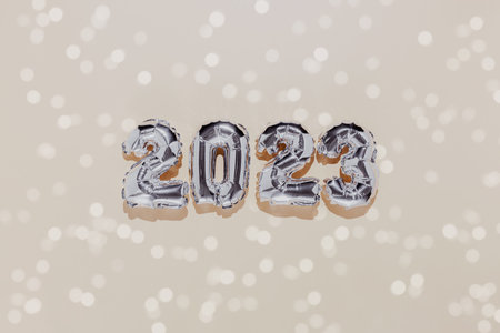 Christmas or New Year background. Beige color flat lay decorated with white paper glitter and silver shiny 2023 baloon numbers. Simple minimalistic greeting card.の写真素材