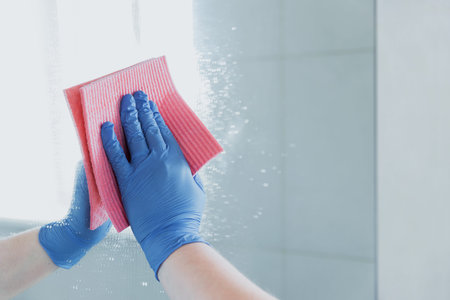 Cropped view of housekeeper woman hand in blue rubber glove polishing, cleaning, swiping mirror with...
