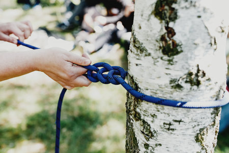 Women hands pull a strong blue rope tied to a birch tree. Professional zip line or cable car installation. Time for fun and relaxation. Family weekends activity together. High quality photoの写真素材