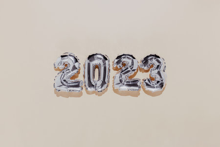 Christmas or New Year background. Beige color flat lay with silver shiny 2023 balloon numbers in the center. Simple minimalist greeting card.の写真素材
