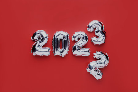 Christmas or New Year background. Red color flat lay with silver shiny 2023 balloon numbers in the center. Simple minimalist greeting card.の写真素材