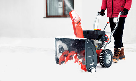 Snow blower powered by gasoline in action. Man outdoor in front of house using snowblower machine. Snow removal, thrower assistant in winter outside home. Young worker guy blowing snow during blizzardの写真素材
