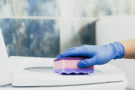 Close up on woman hand gloved in blue rubber protective gloves. Housewife cleaning toilet bowl, seat with detergent liquid, wet wipe in bathroom, restroom. Female washing, disinfecting toilet seatの写真素材