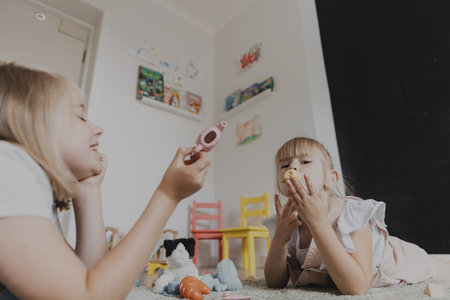 Close-up of female children playing with colorful toy play tea set. Kids lying on carpet at home...