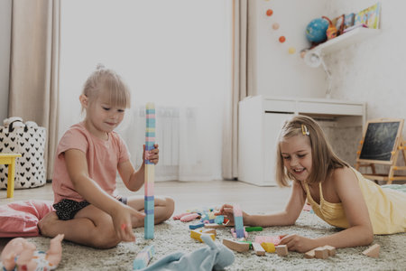 Children playing with colorful toys. Kids sitting on carpet at home bedroom or kindergarten, nursery. Educational eco-friendly game for child. Cute little sisters build house, tower, having funの写真素材