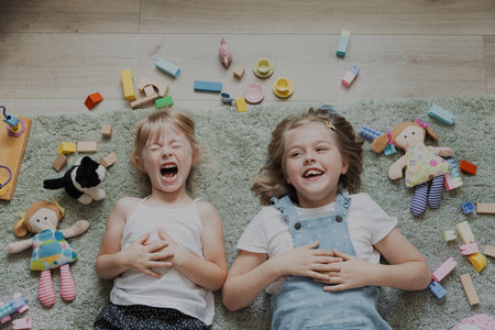 Top view from above on children playing with colorful toys. Portrait of kids lying on carpet at home bedroom or kindergarten. Two happy smiling sisters. Educational eco-friendly gamesの写真素材