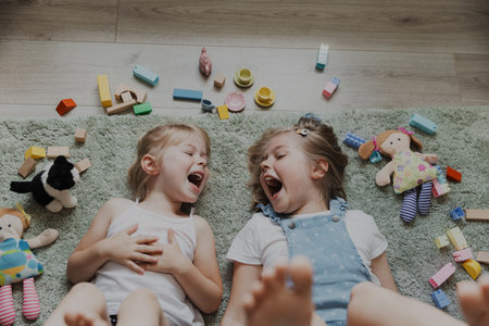 Top view from above on children playing with colorful toys. Portrait of kids lying on carpet at home bedroom or kindergarten. Two happy smiling sisters. Educational eco-friendly gamesの写真素材
