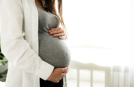 Mid-section portrait of pregnant woman or lady holding her baby bump or belly with hands. Standing...