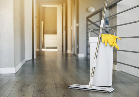 Cleaning supplies: mop, gloves, bucket with wringer sitting on wooden laminate floor in modern living room, wet equipment tools, housekeeping concept. Emphasizing home sanitation, cleanliness, hygieneの写真素材