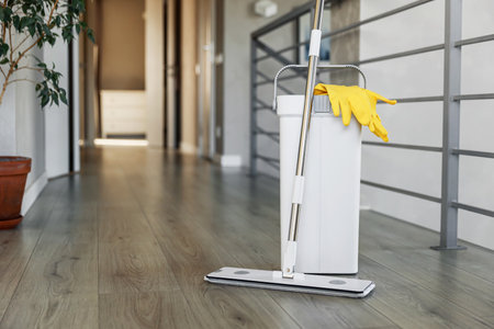 Cleaning supplies: mop, gloves, bucket with wringer sitting on wooden laminate floor in modern living room, wet equipment tools, housekeeping concept. Emphasizing home sanitation, cleanliness, hygieneの写真素材