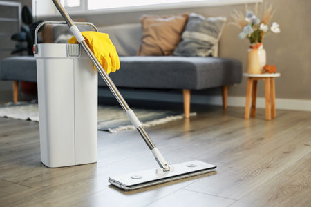 Cleaning supplies: mop, gloves, bucket with wringer sitting on wooden laminate floor in modern living room, wet equipment tools, housekeeping concept. Emphasizing home sanitation, cleanliness, hygieneの写真素材